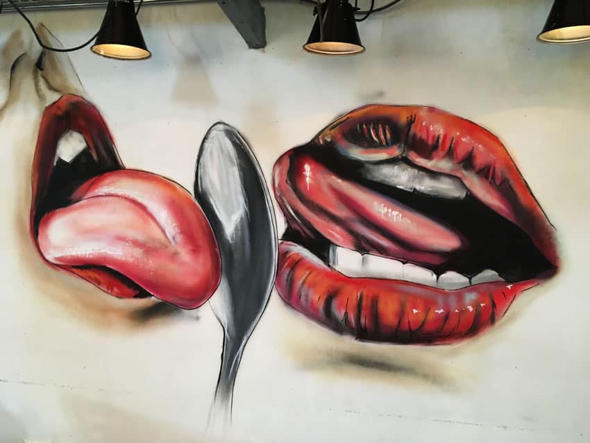 muurschildering van likkende tong en lippen en lepel spuitbus en stift op acryl en waterbasis kleurrijk gemaakt door Timbert